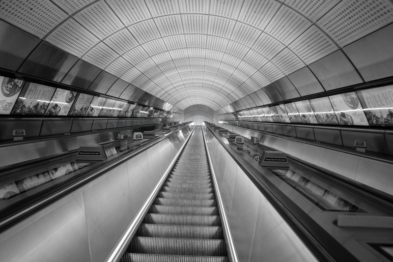 An empty escalator rises through a ribbed, tiled vault toward a bright opening.