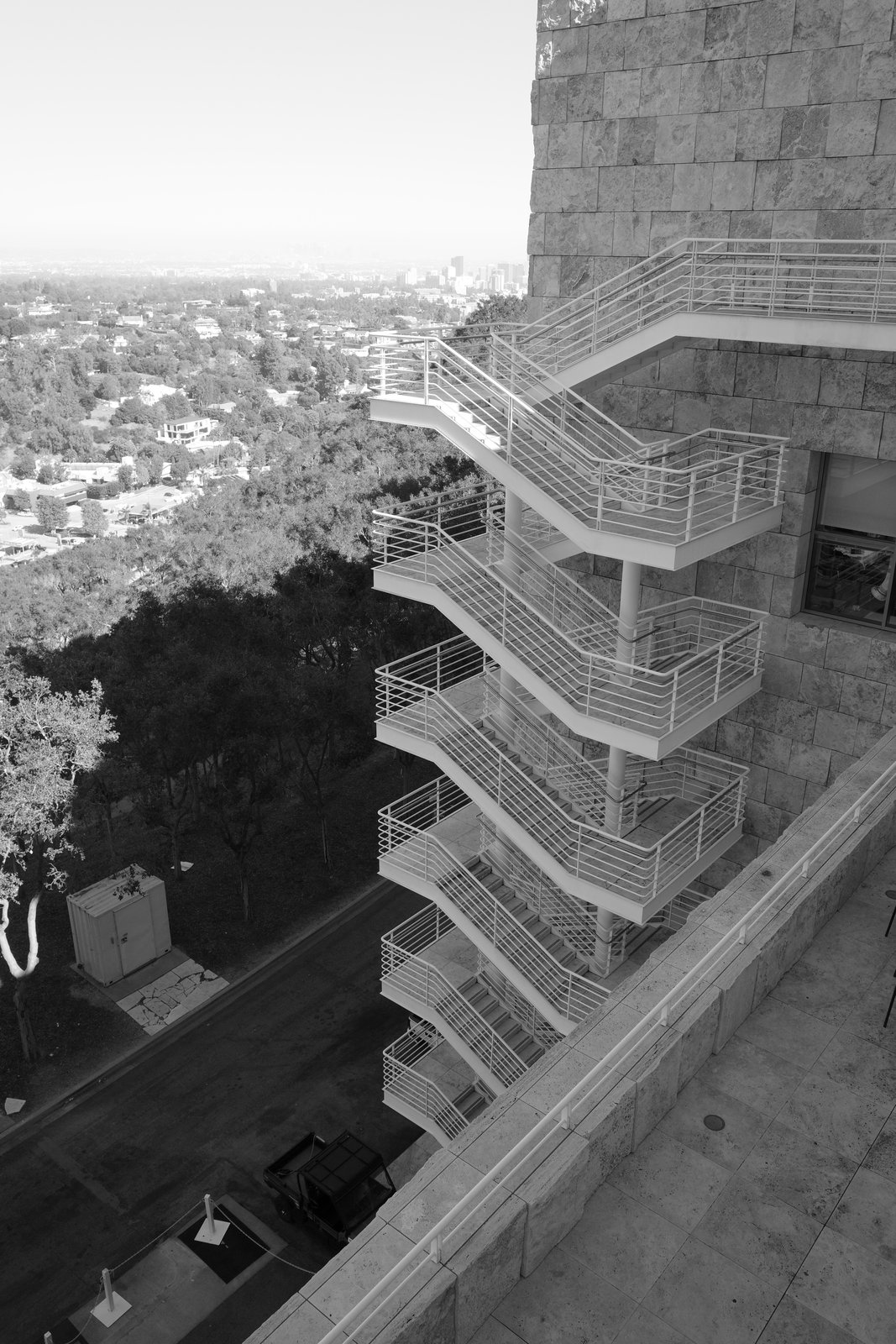 Exterior stairs zigzag down beside stone walls and trees.