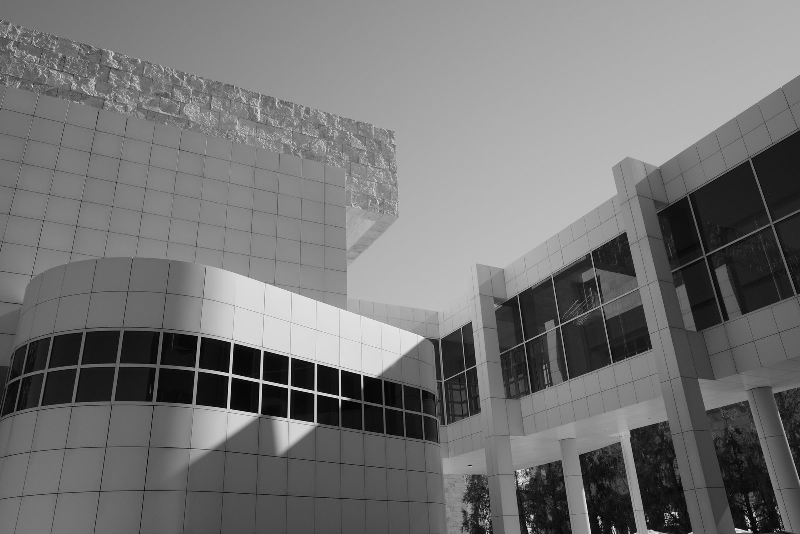 A diagonal shadow crosses a curved white facade beside a grid of dark windows.