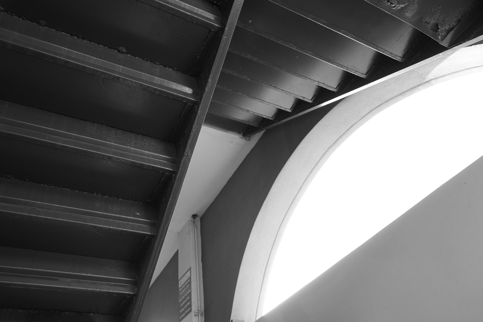 A bright arch crosses the dark underside of a staircase.