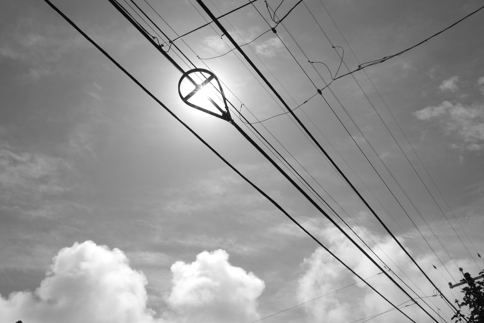 The sun aligns with a loop in overhead trolley wires beneath clouds.