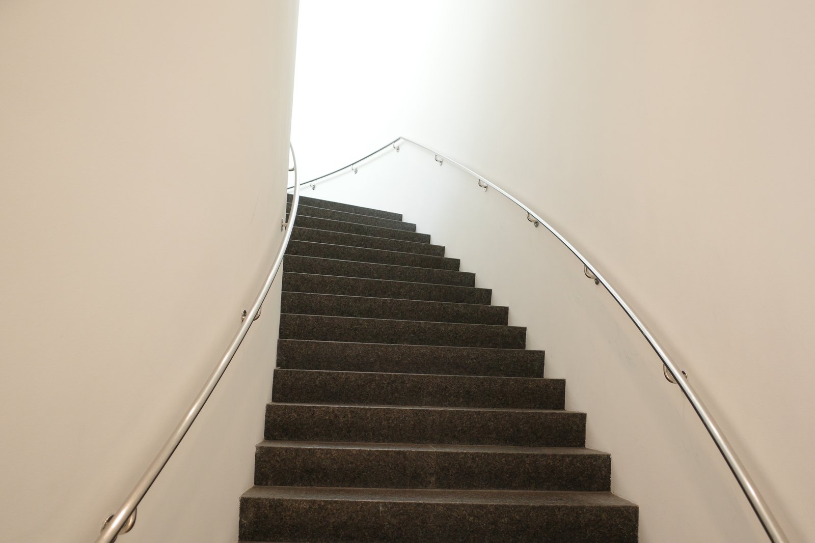 An empty curved stairwell rises toward a bright opening.