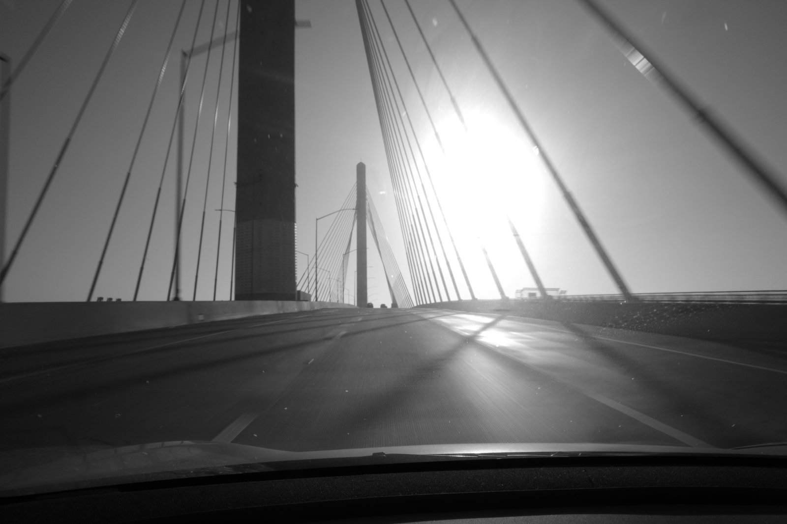 Bridge cables cross bright flare and a blurred roadway.