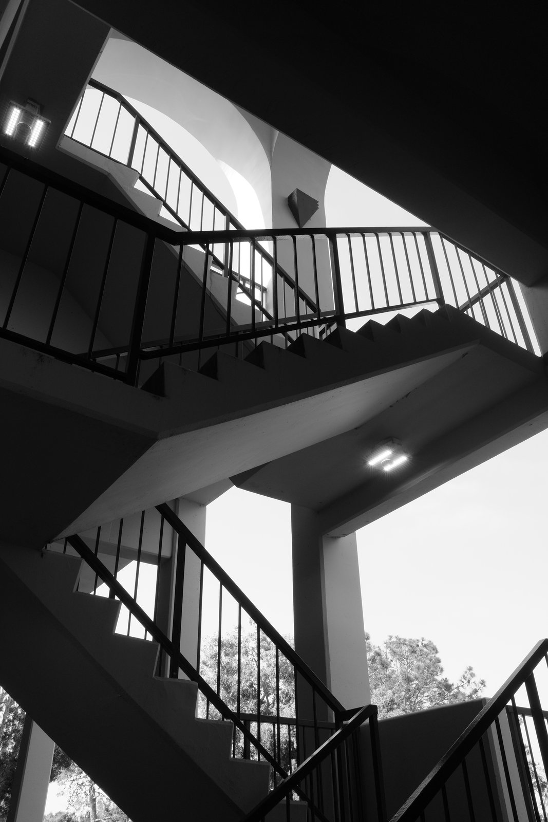 Zigzag stair flights and dark railings cross openings of sky.