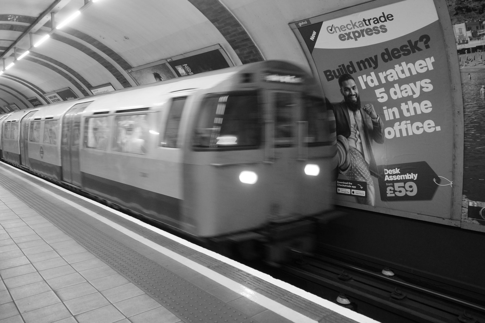 A blurred Underground train passes a tiled station platform.