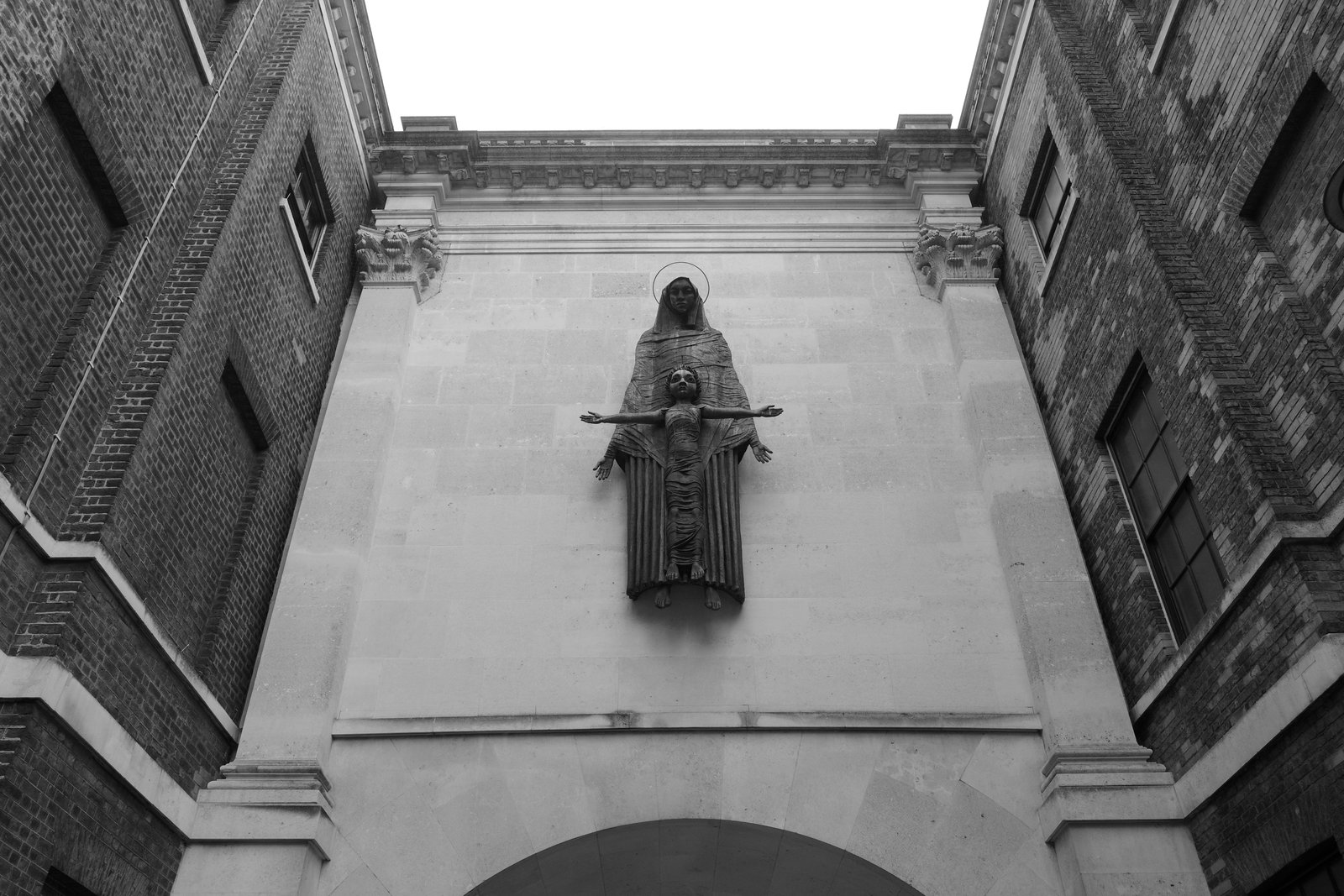 A statue hangs above an arch between brick walls.