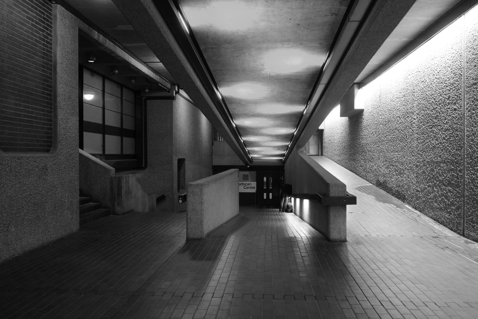Wall lights and ceiling reflections lead down a covered concrete passage.