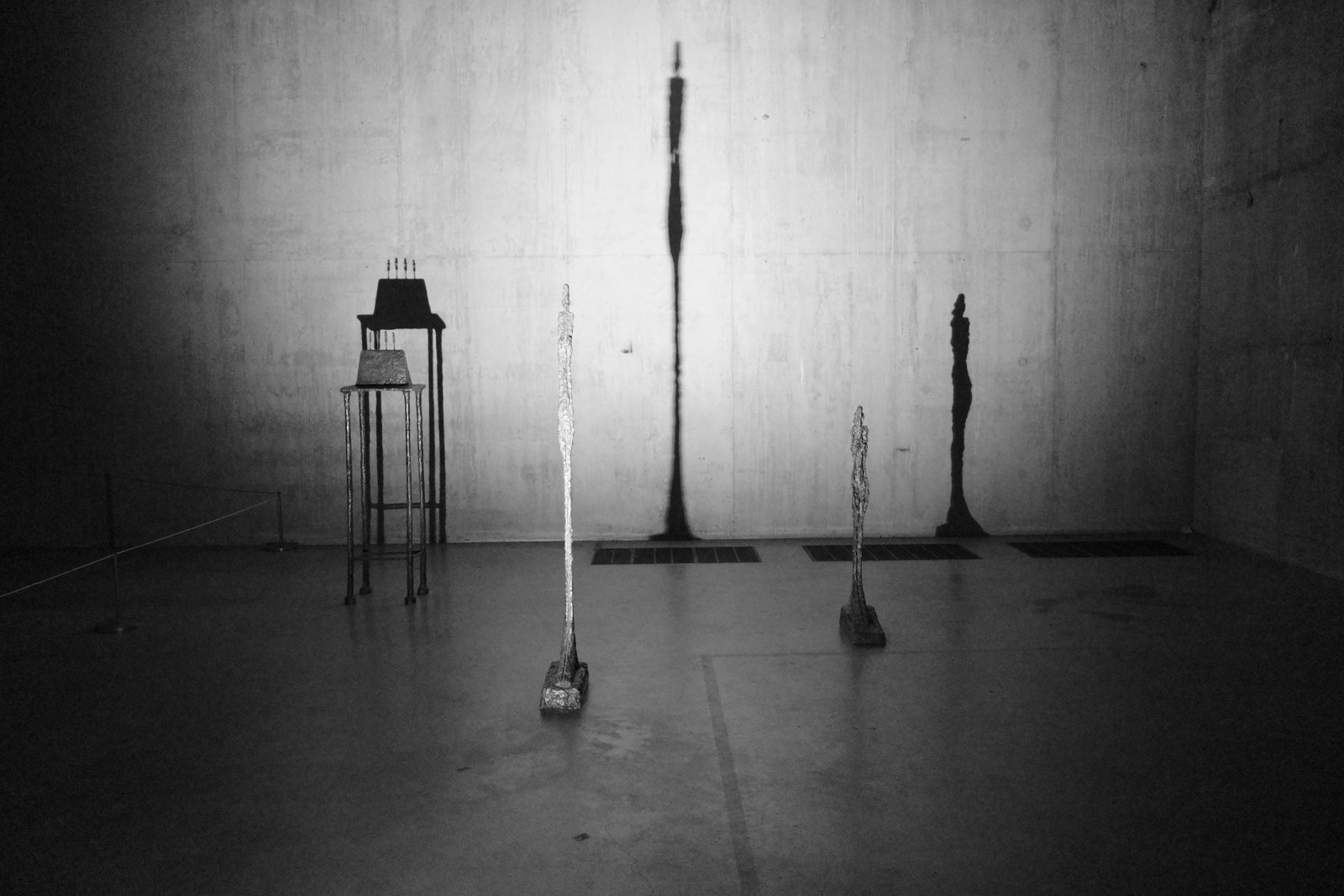 Thin sculptures cast elongated shadows across a dim room.
