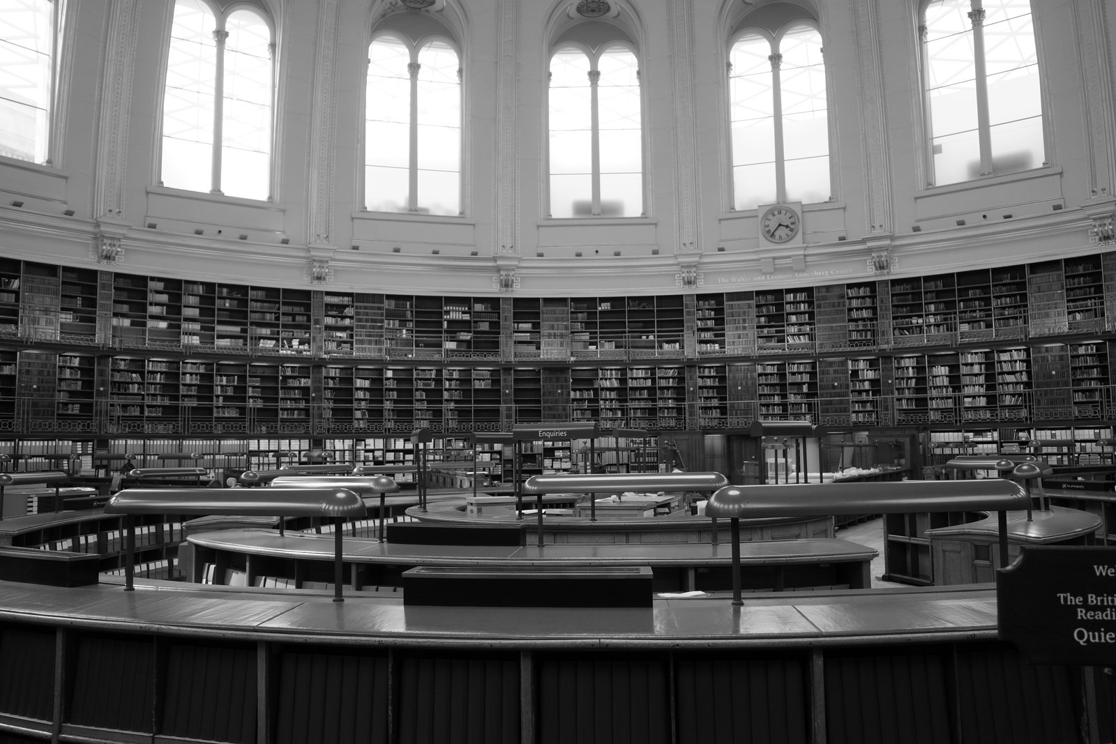 Curved desks and bookshelves sit beneath bright arched reading-room windows.