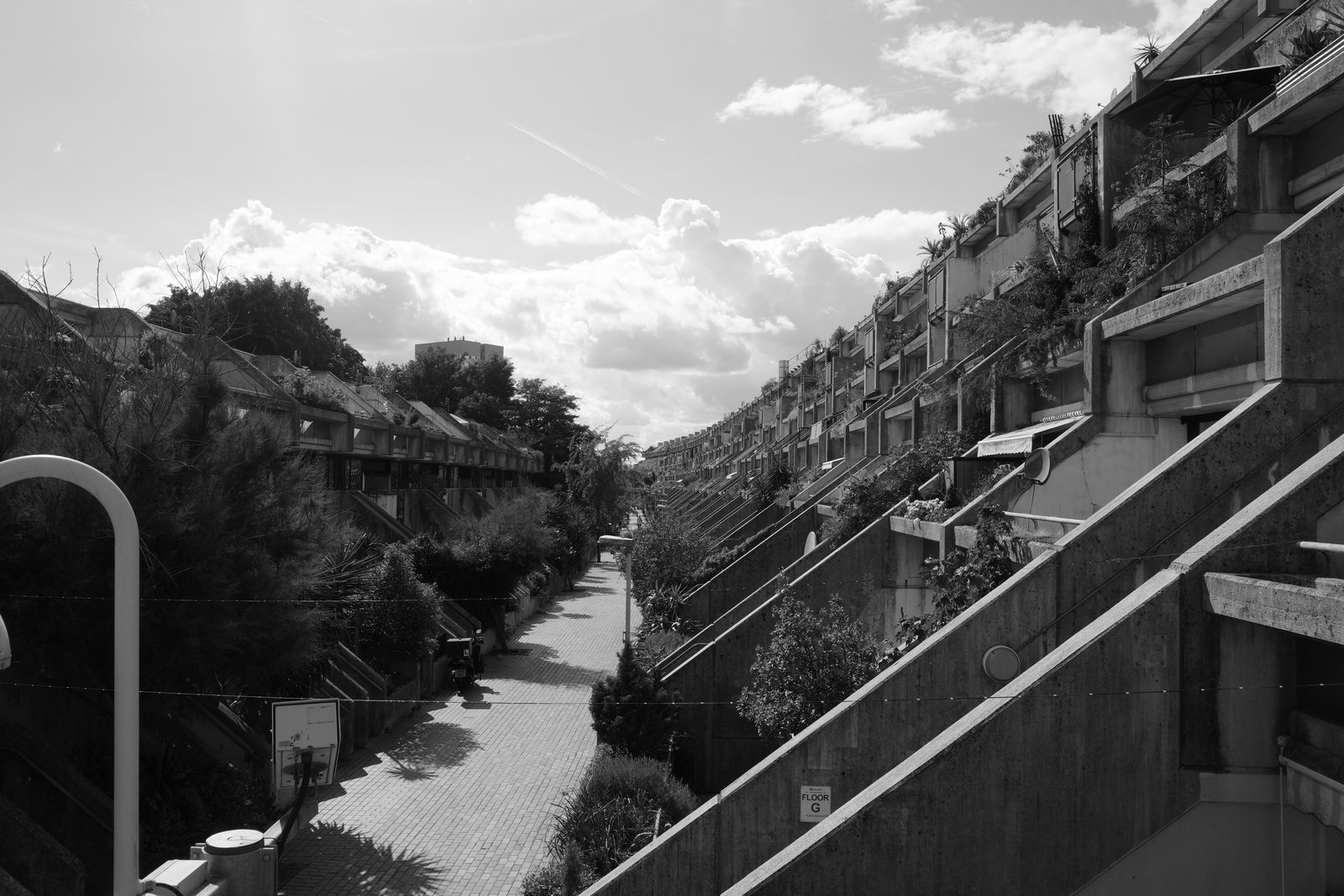 Terraced concrete housing and plants line a long walkway.