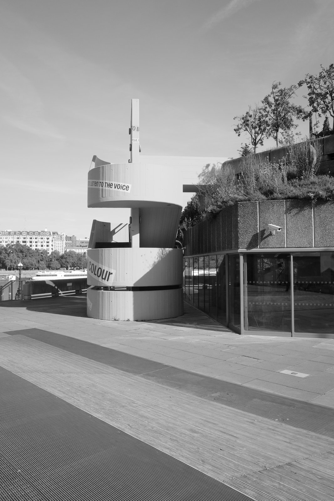 A freestanding spiral stair rises beside a concrete building against open sky.
