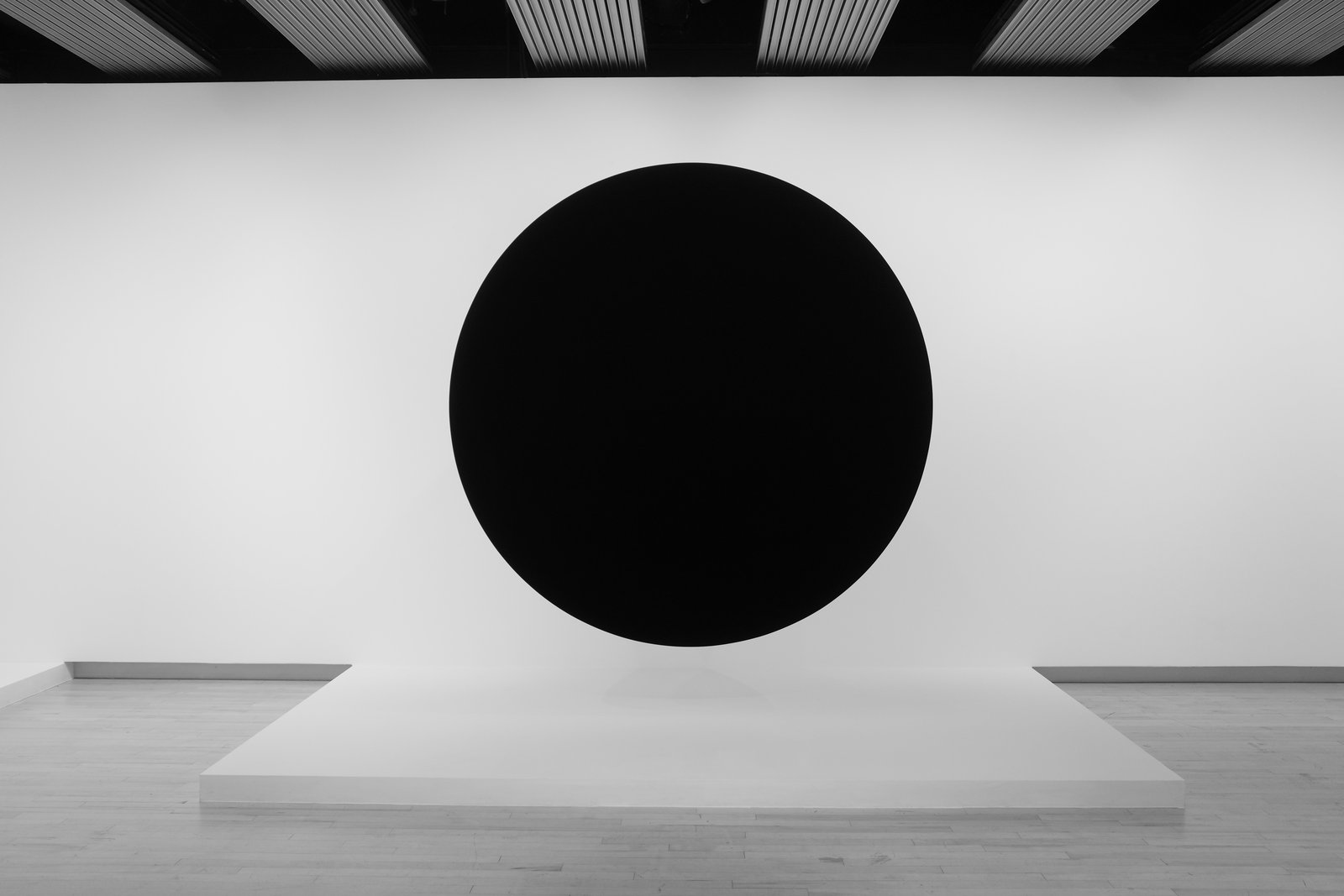 A black circular opening sits within a white gallery wall above a platform.
