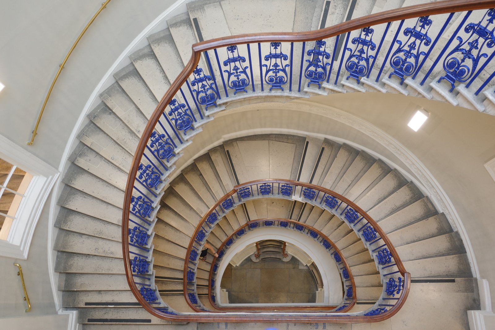 Blue balustrades descend around repeated curves of a stone stairwell.
