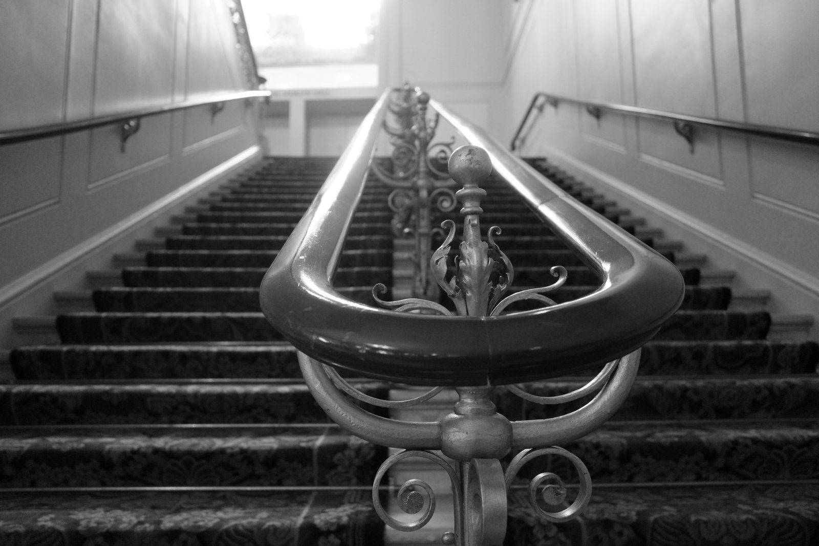 A polished looping handrail leads up dark worn steps toward a bright landing.