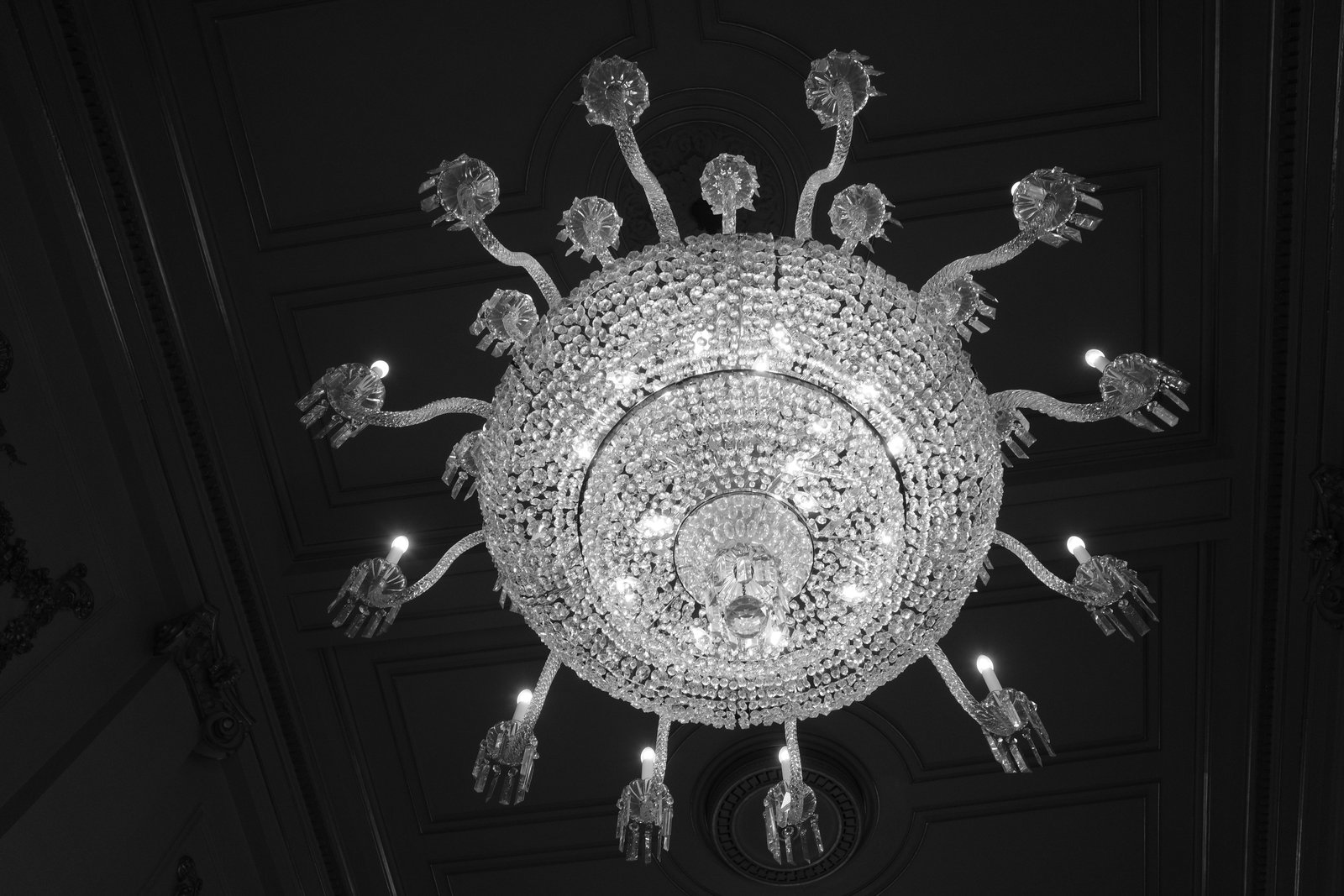 A circular crystal chandelier hangs against a dark ceiling.