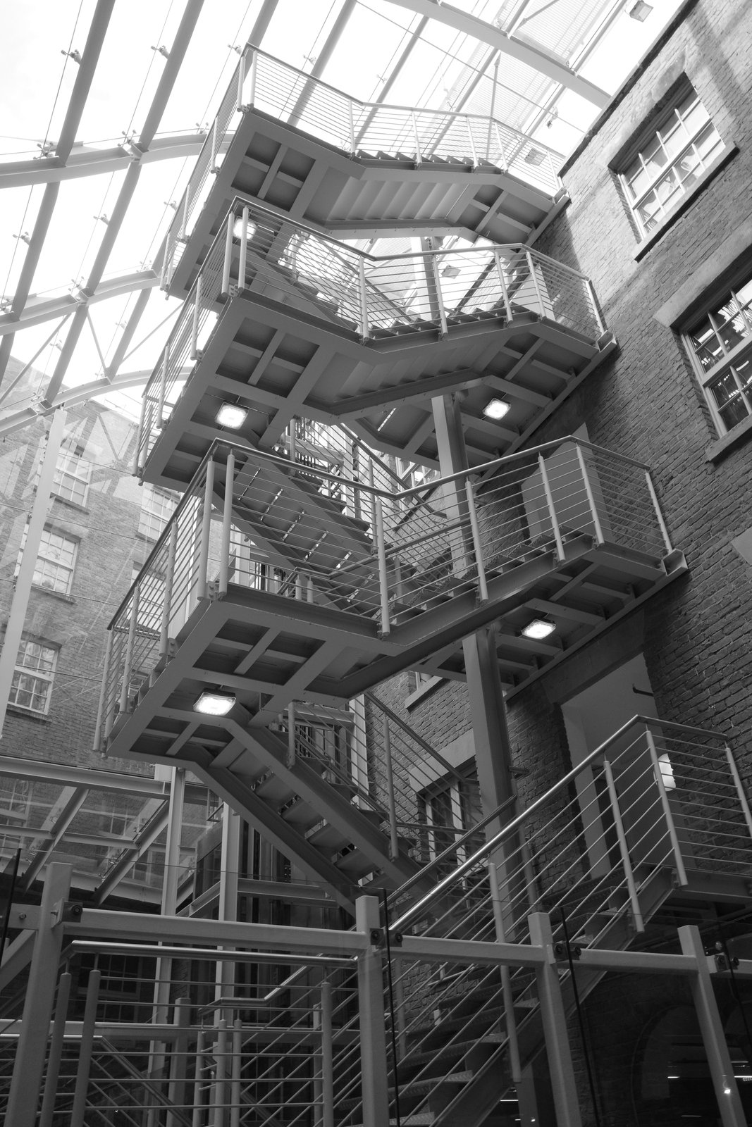 External steel stair flights stack between brick walls and a glazed roof.