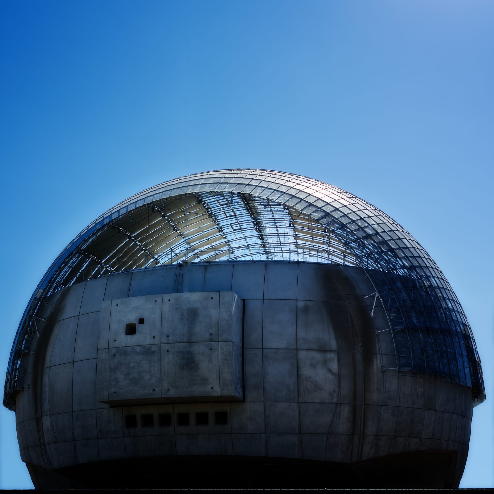 A domed building of concrete and glass against a clear blue sky.