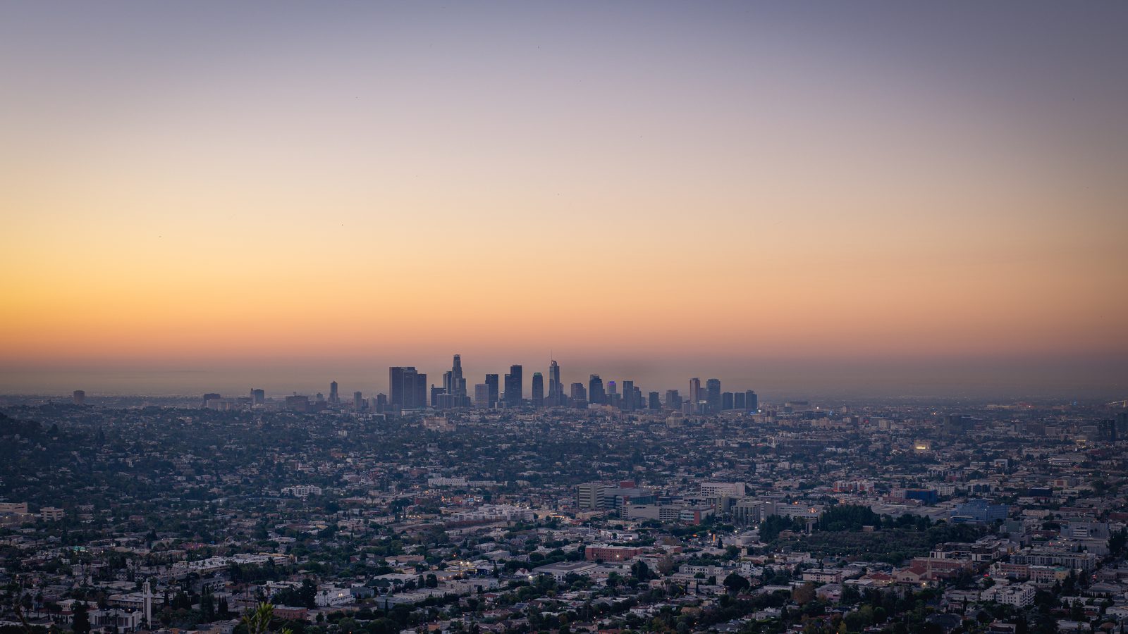 A downtown skyline rises from a flat sprawl of low buildings under a hazy dawn sky.