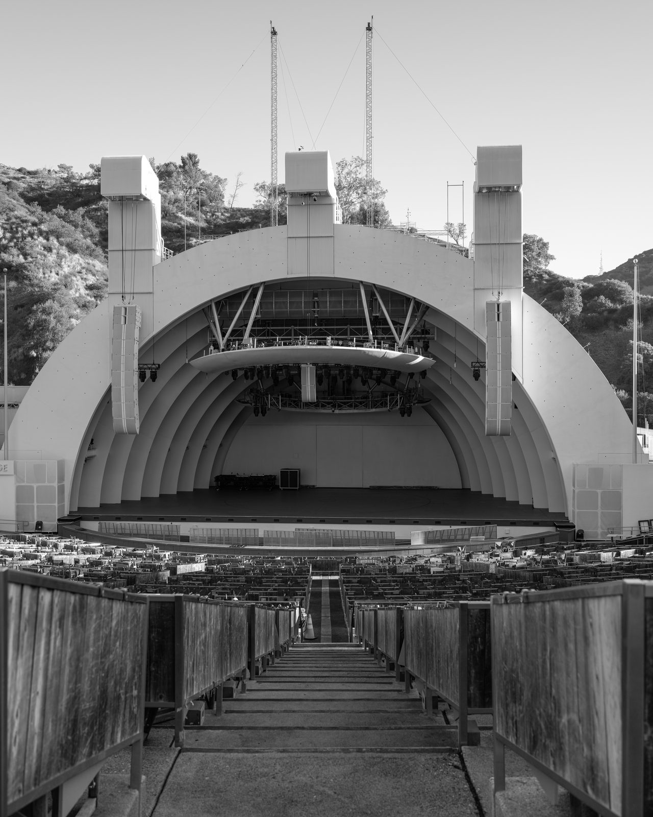 An empty amphitheater looks up a center aisle at an arched white band shell with no one on stage.