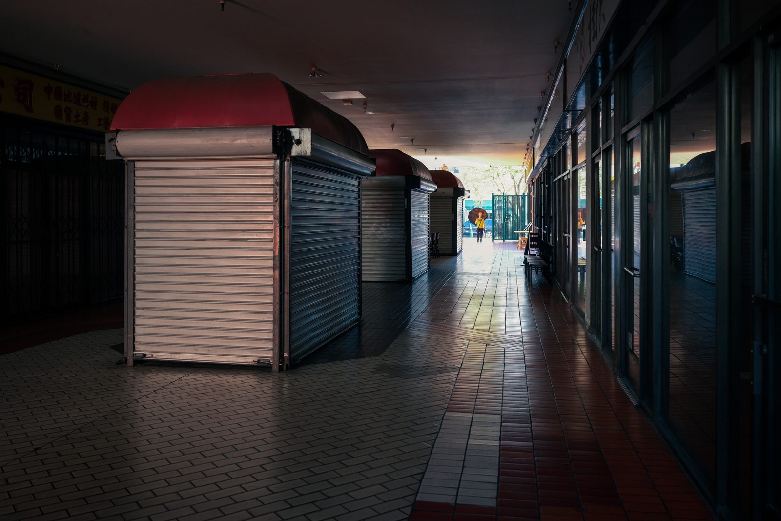 Shuttered market stalls line a dim tiled arcade that opens to daylight at the far end.