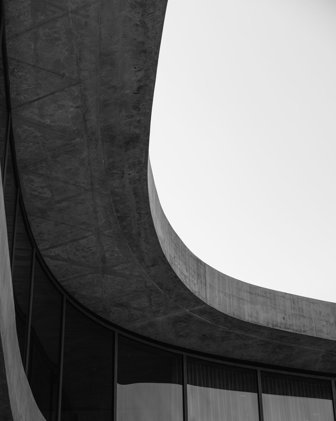 A curved concrete overhang sweeps across a pale sky above a band of windows.