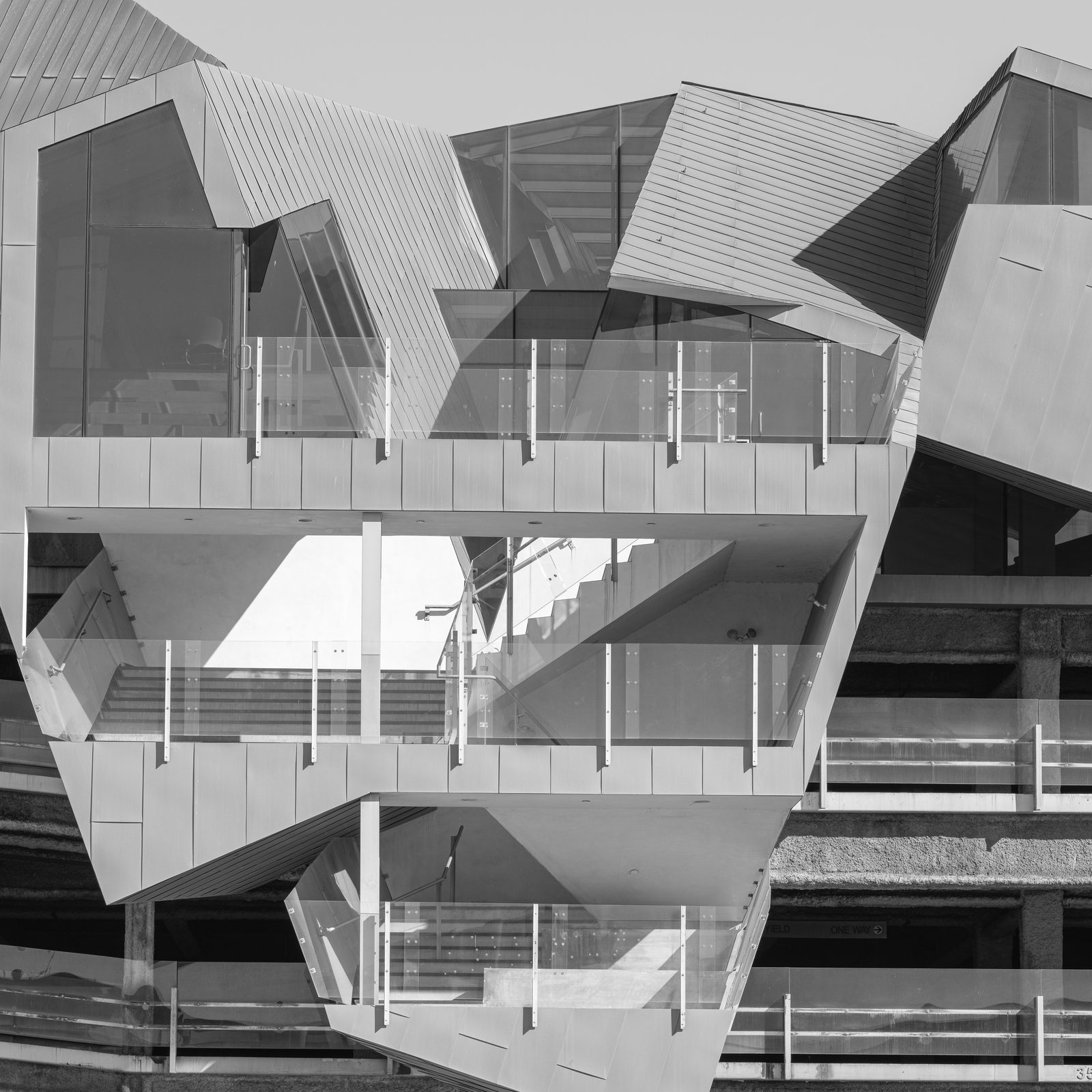 A building's faceted metal skin folds around stacked balconies with glass railings.