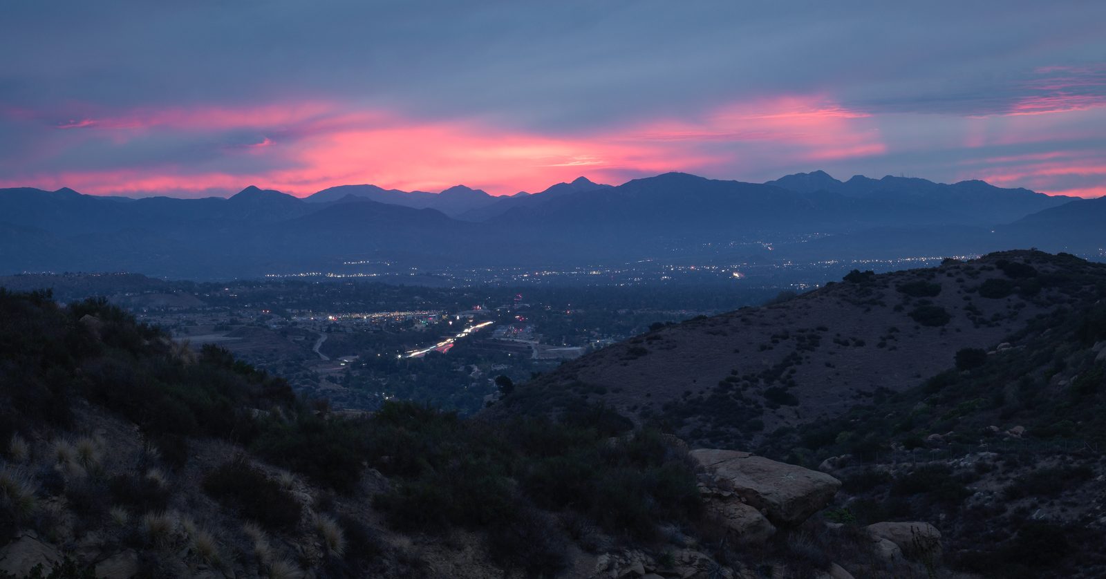 A valley of lights at dusk under mountains, with the last red of sunset along the ridge.
