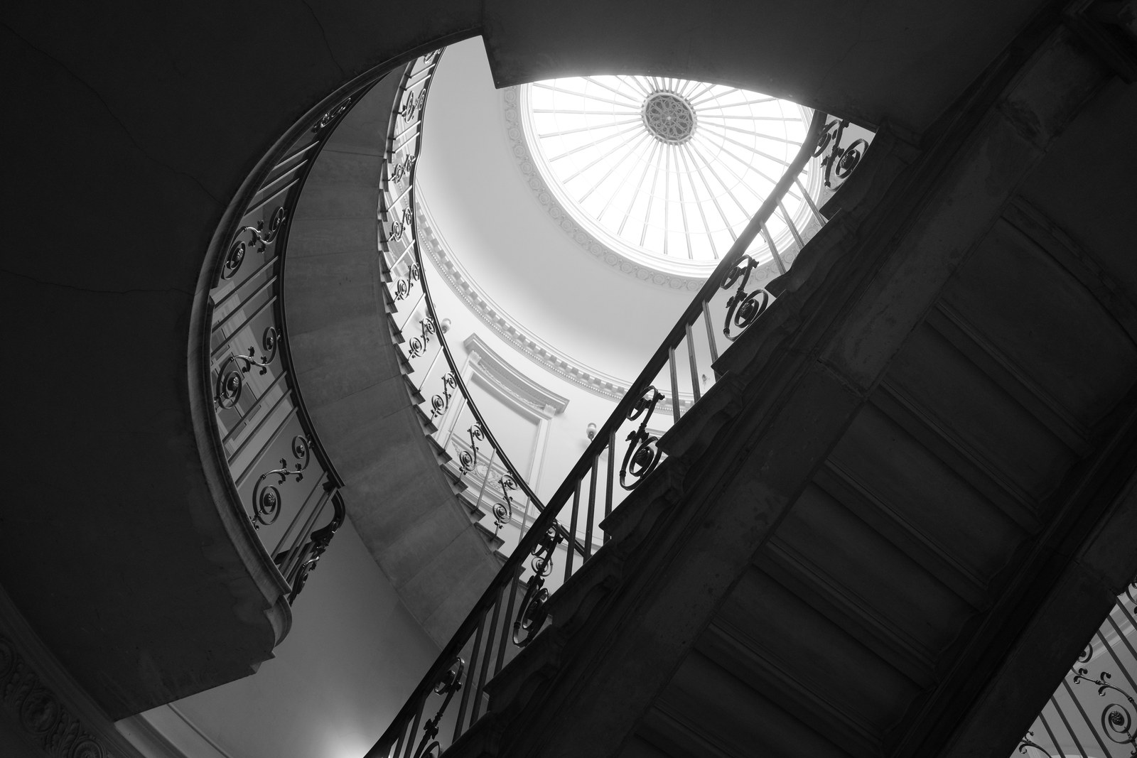 Dark curving stairs rise toward a bright circular skylight.