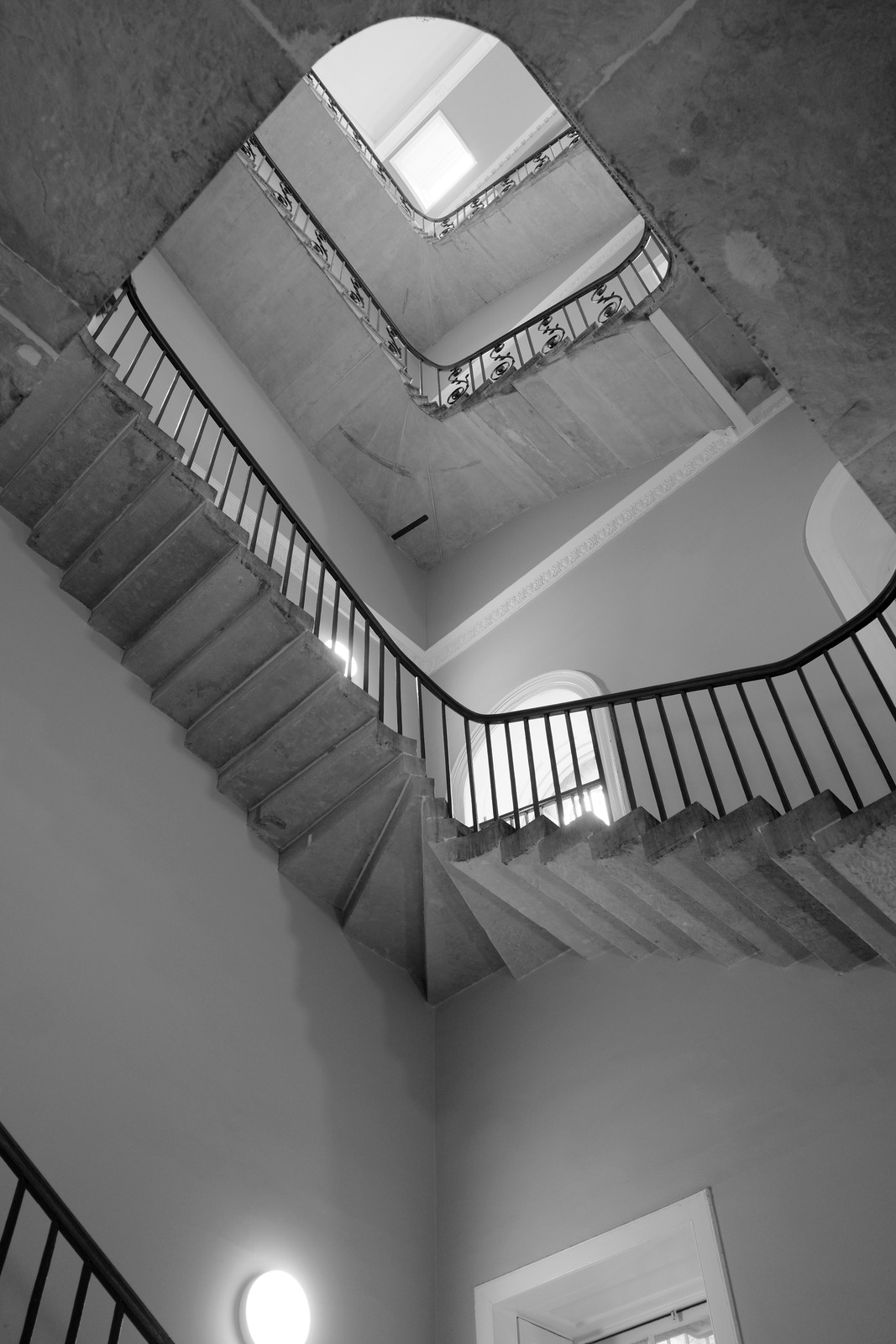 A square stairwell rises diagonally toward a bright roof opening.