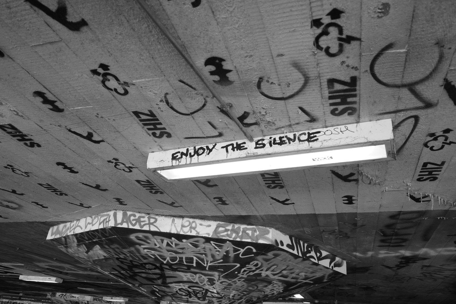 A fluorescent fixture marked Enjoy the Silence hangs beneath a graffiti-covered ceiling.