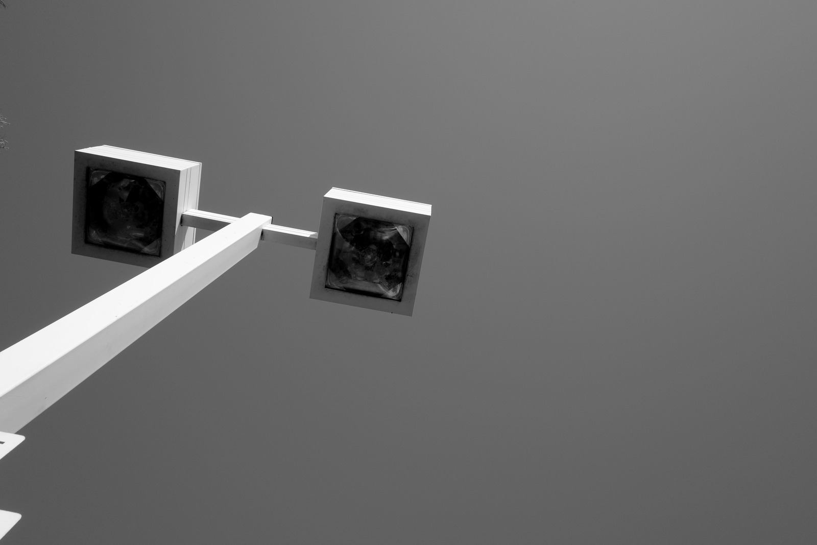 Two square lamps sit atop a pale pole against open sky.
