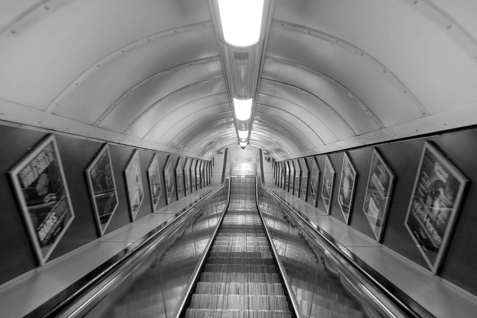 An empty escalator descends beneath curved ceiling panels and framed advertisements.