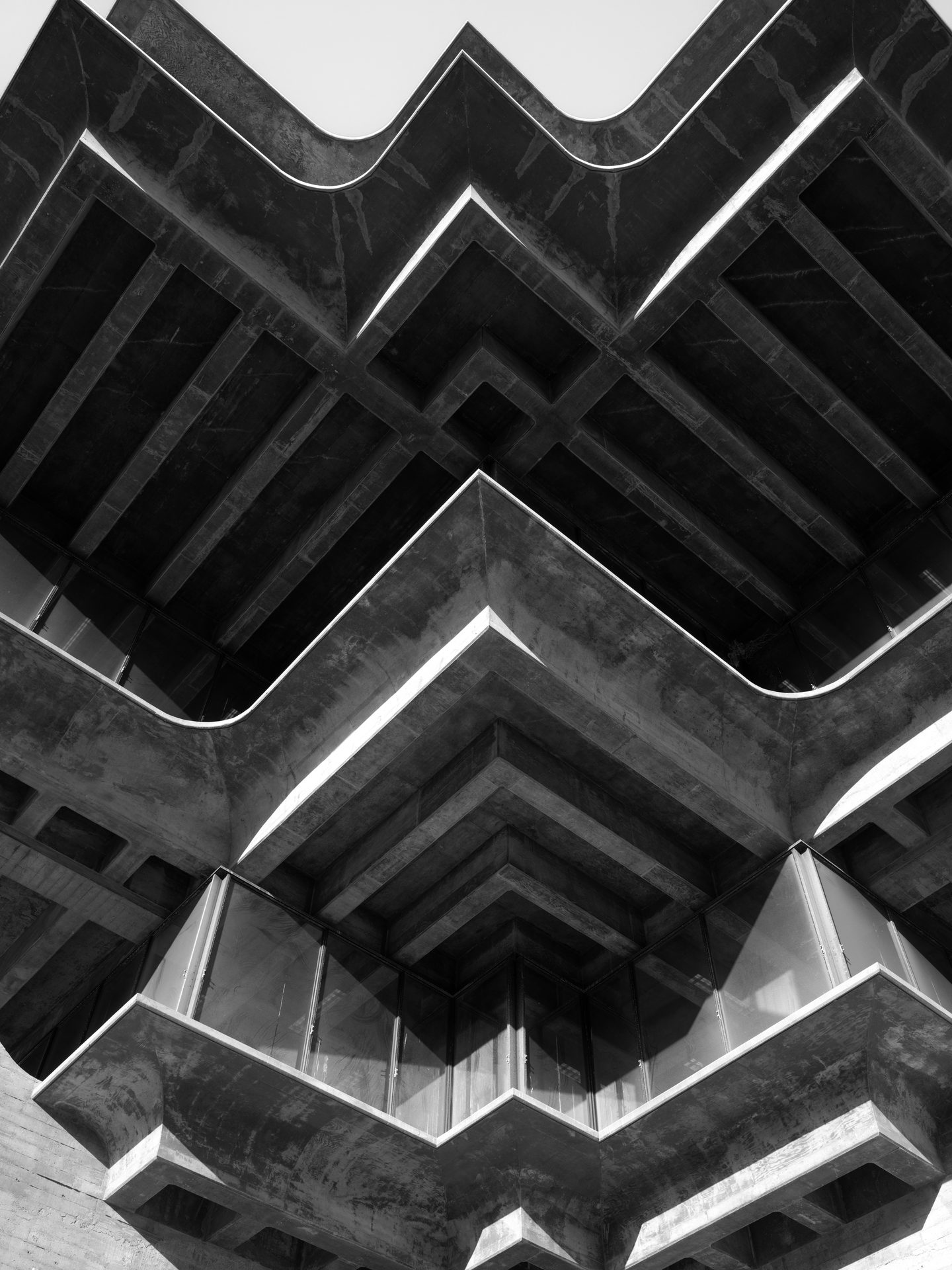The underside of a concrete library cantilevers outward in stepped chevrons against a white sky.