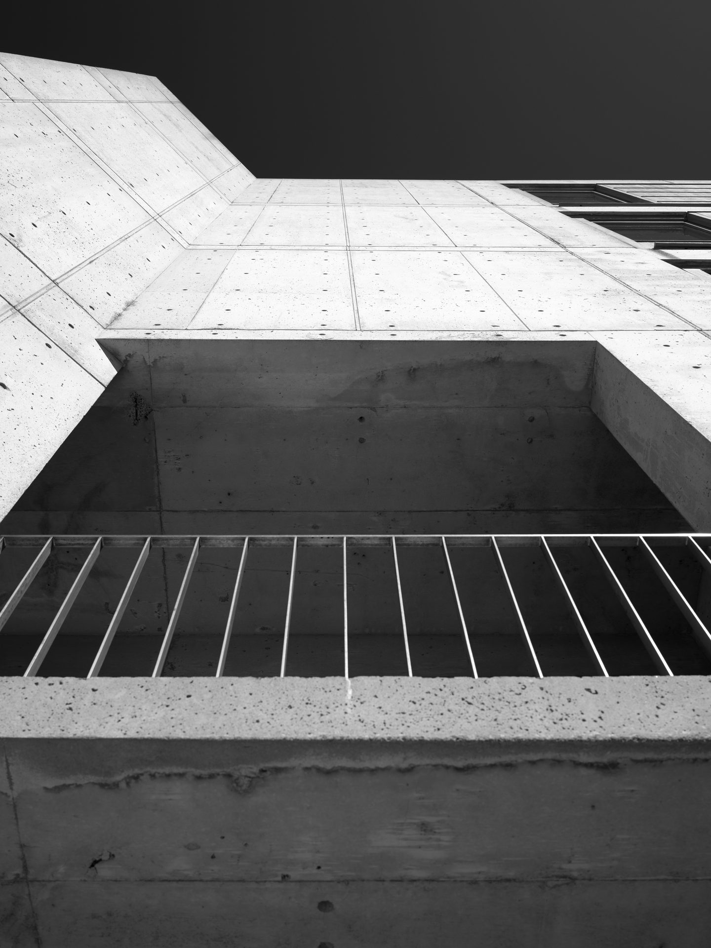 A concrete fin rises toward the sky above a row of white louvers and a dark lintel.