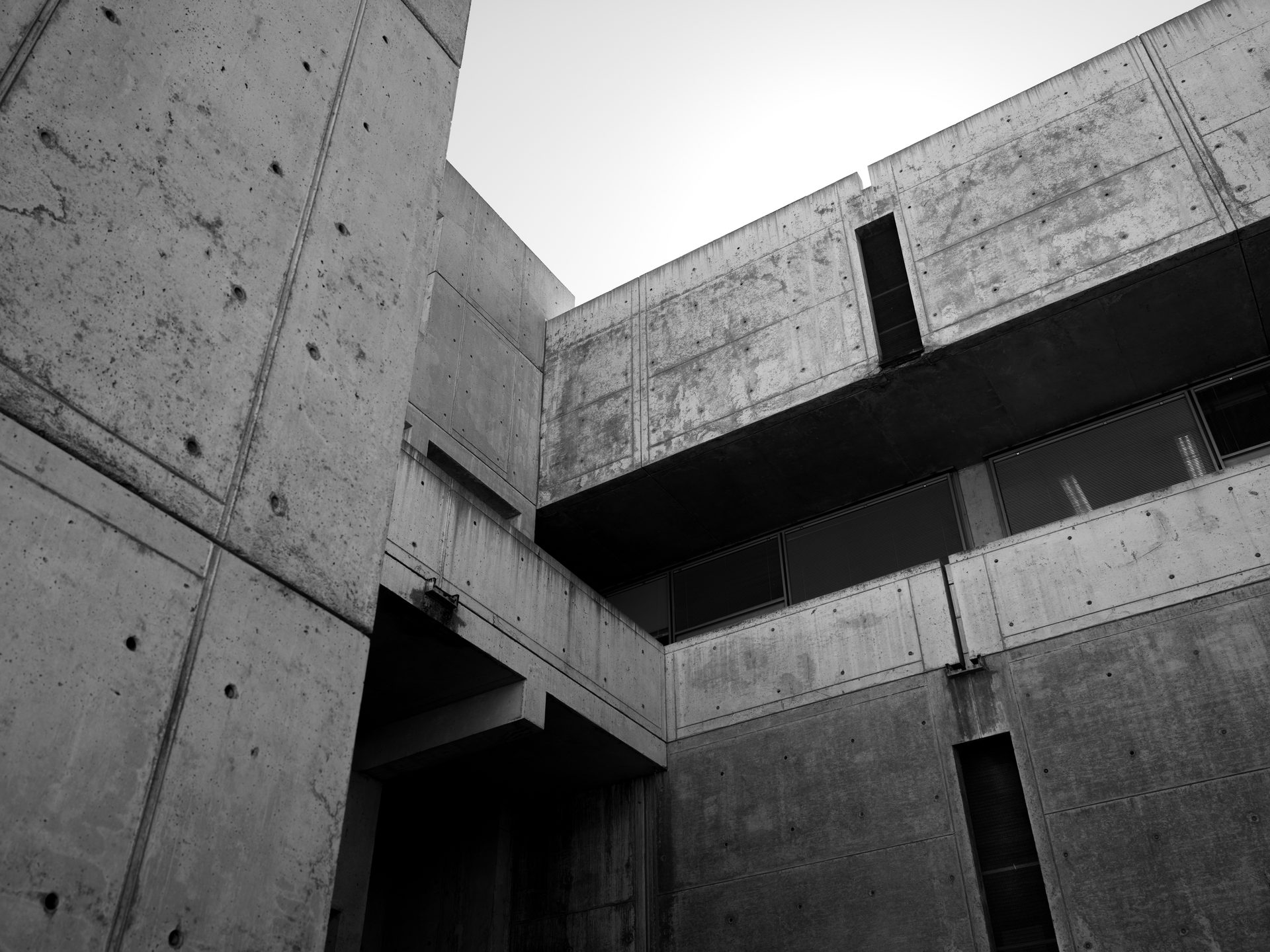 Three concrete masses of a research institute meet at a corner, one face cut by its own shadow under a bright haze.