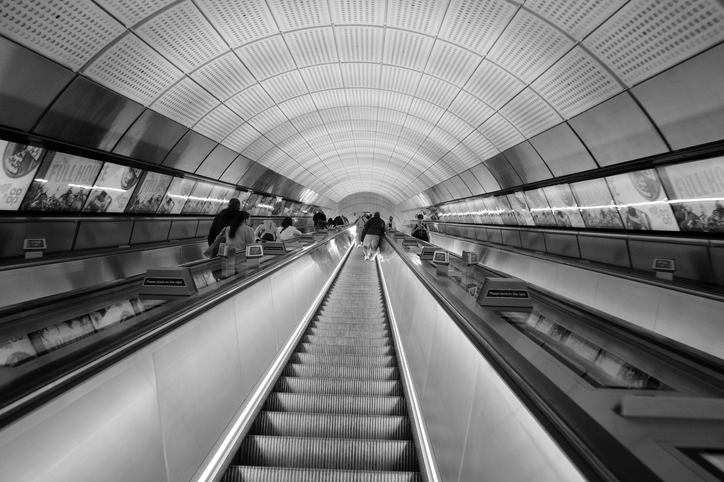 An escalator rises through a ribbed vault beside a few passengers.