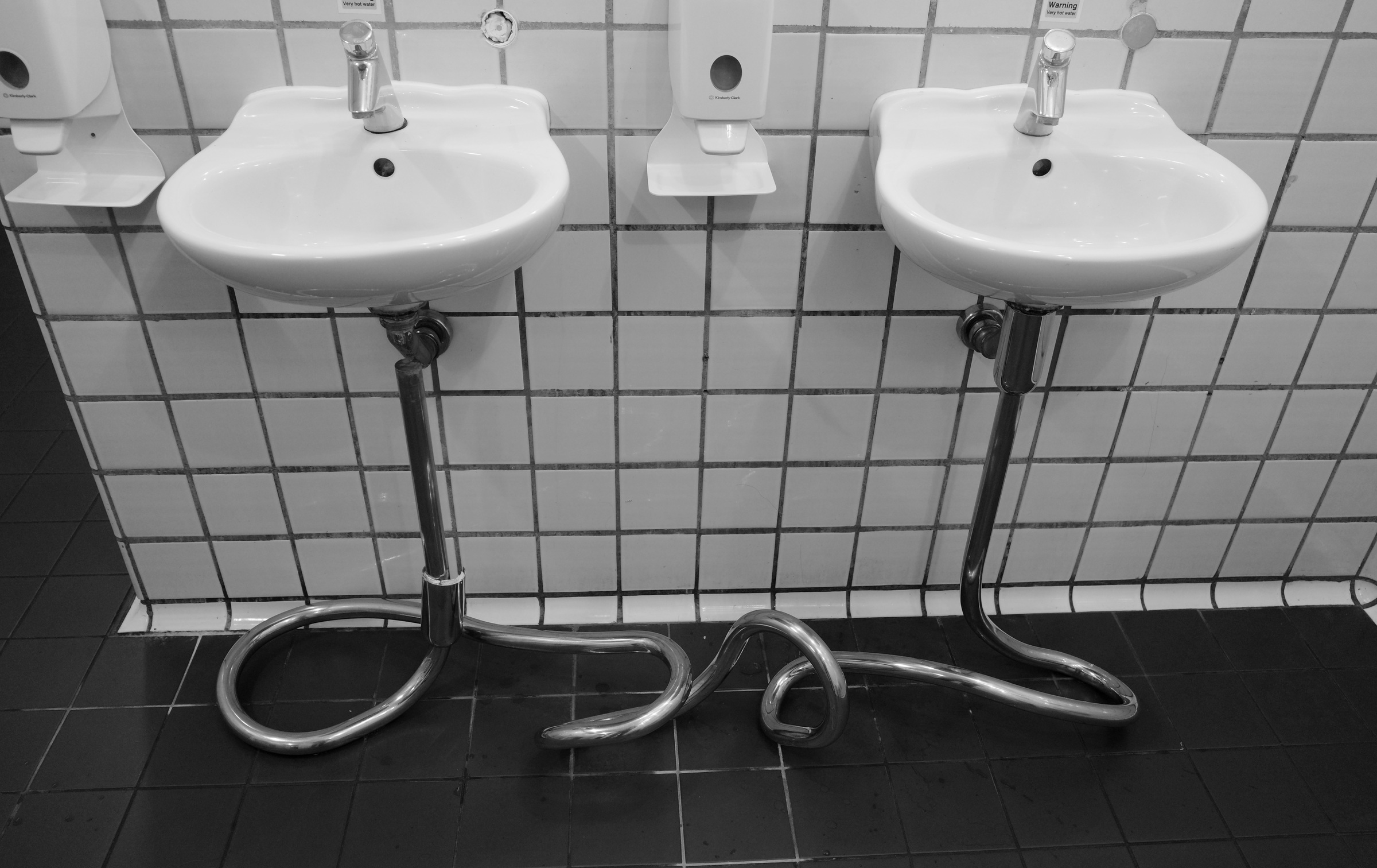 Two white sinks sit above curled metal drainpipes.