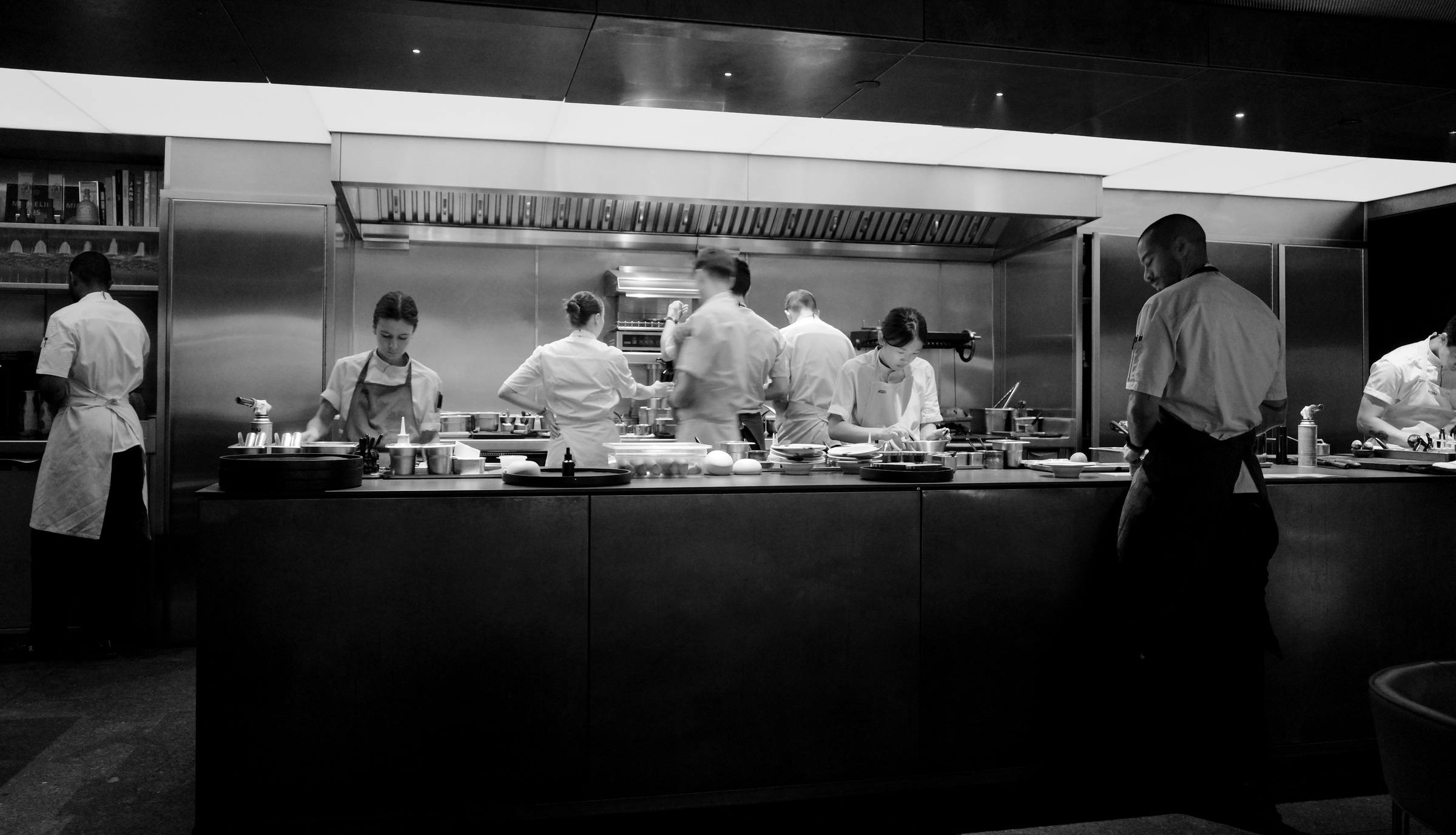 A kitchen team works behind a dark counter beneath a glowing strip of light.
