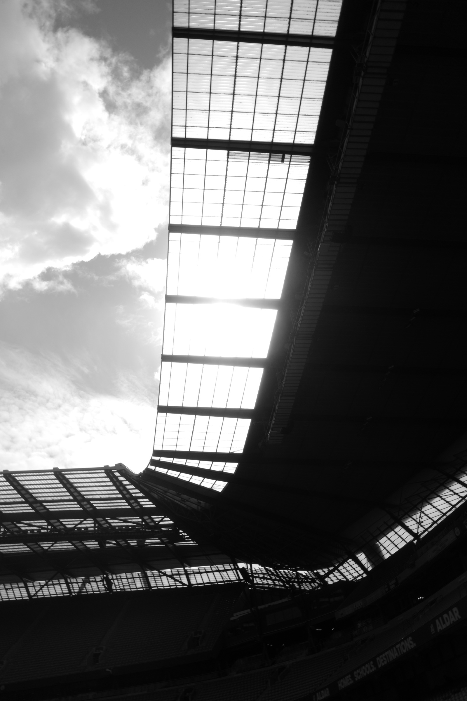 A dark stadium roof curves around a bright opening in the sky.