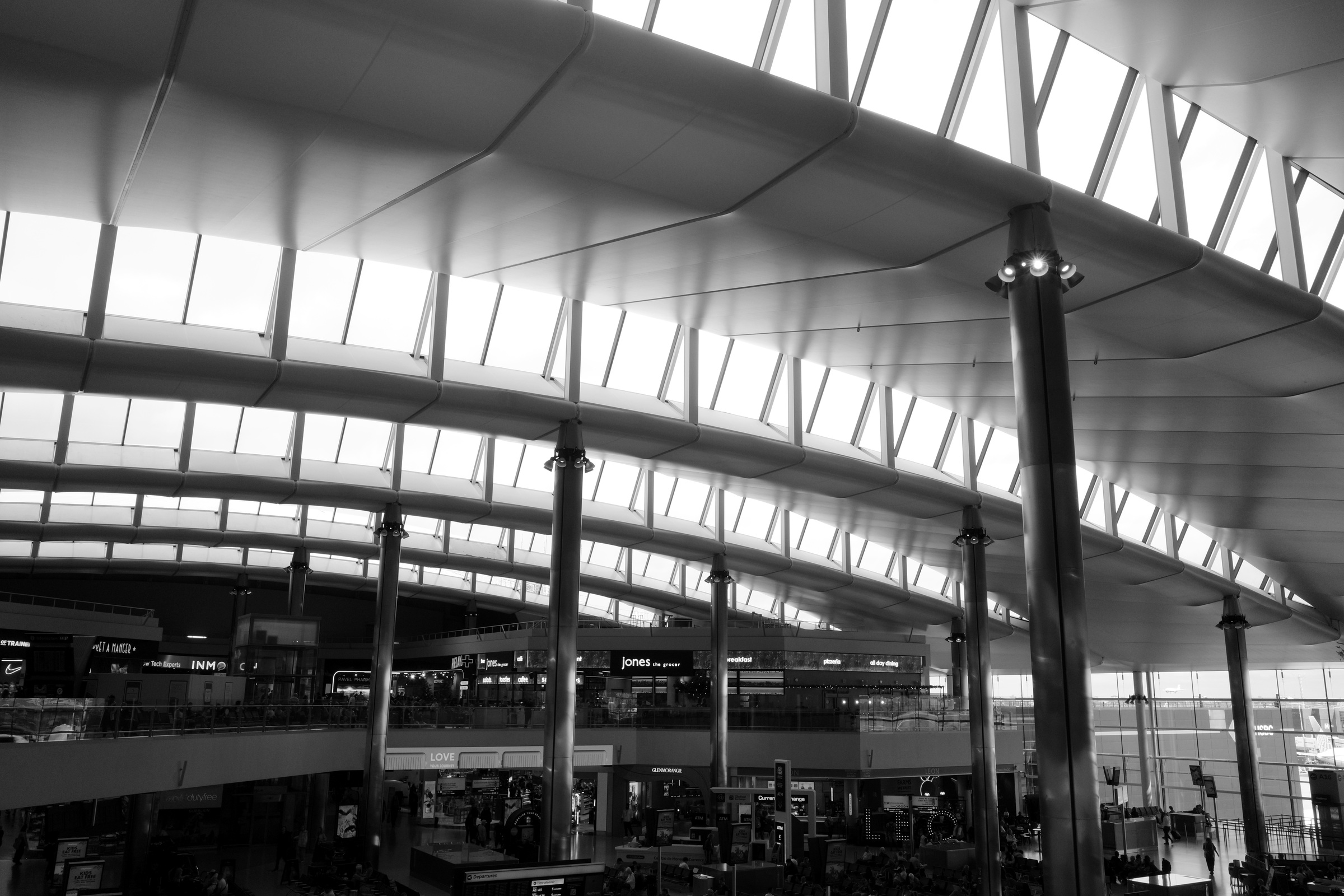 Curved metal panels, columns and glazing span an airport concourse.